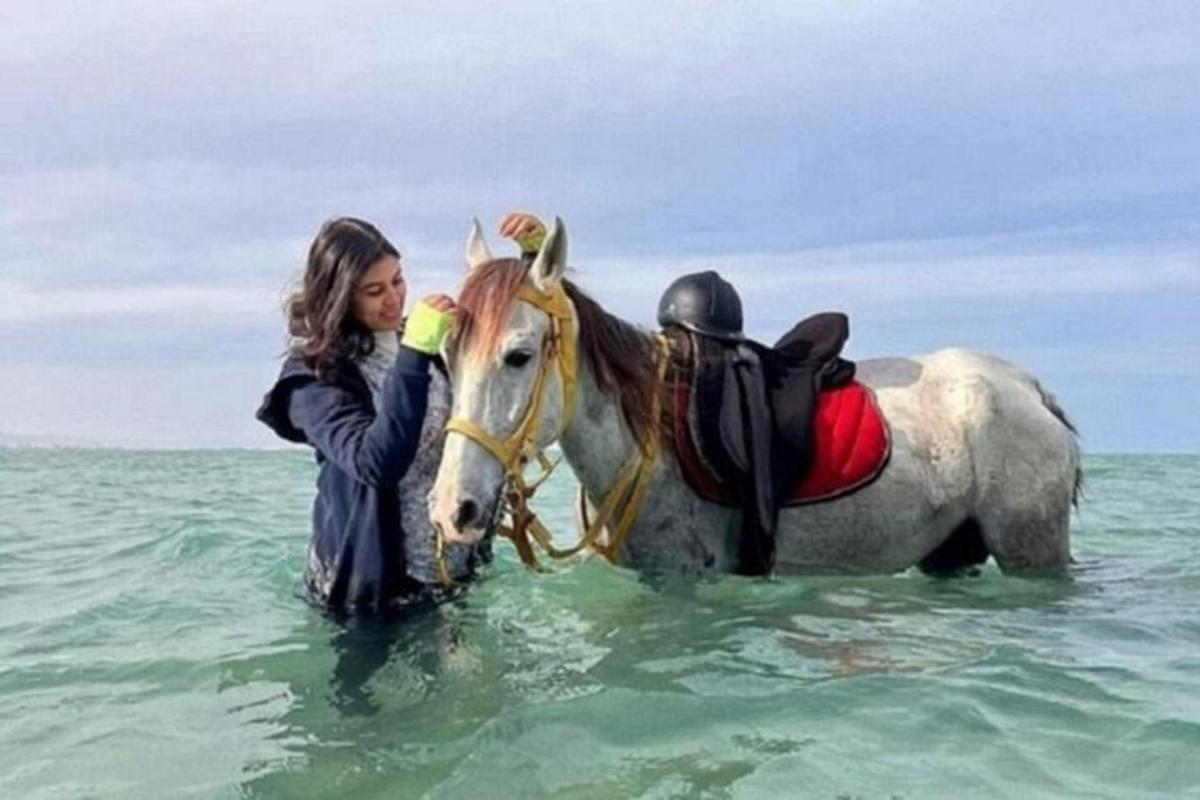 una donna in piedi accanto a un cavallo nell'oceano
