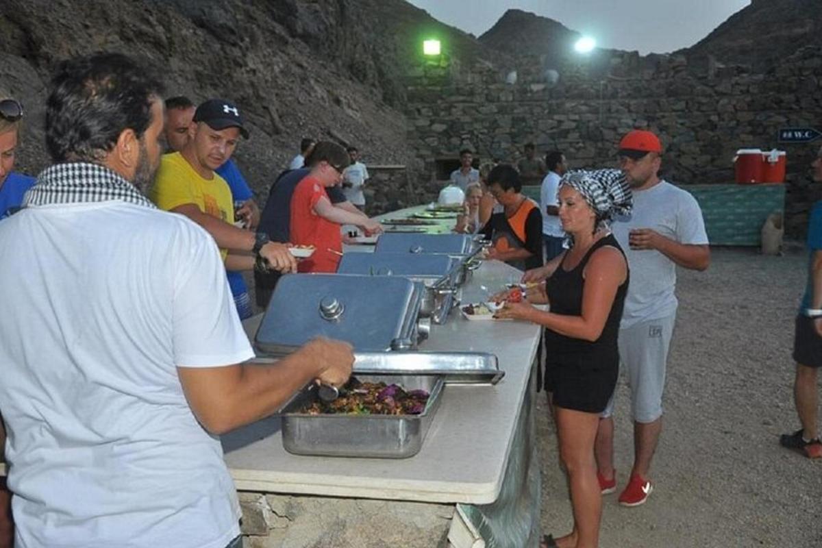 un gruppo di persone in piedi attorno a un tavolo che mangiano cibo