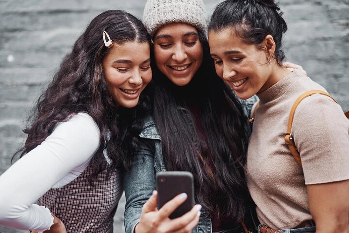 três mulheres rindo enquanto olham para um celular