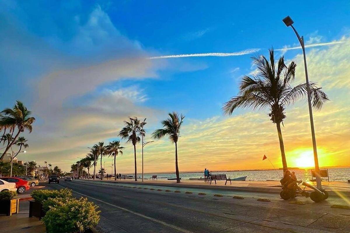 un carrer amb palmeres i l'oceà a la posta de sol