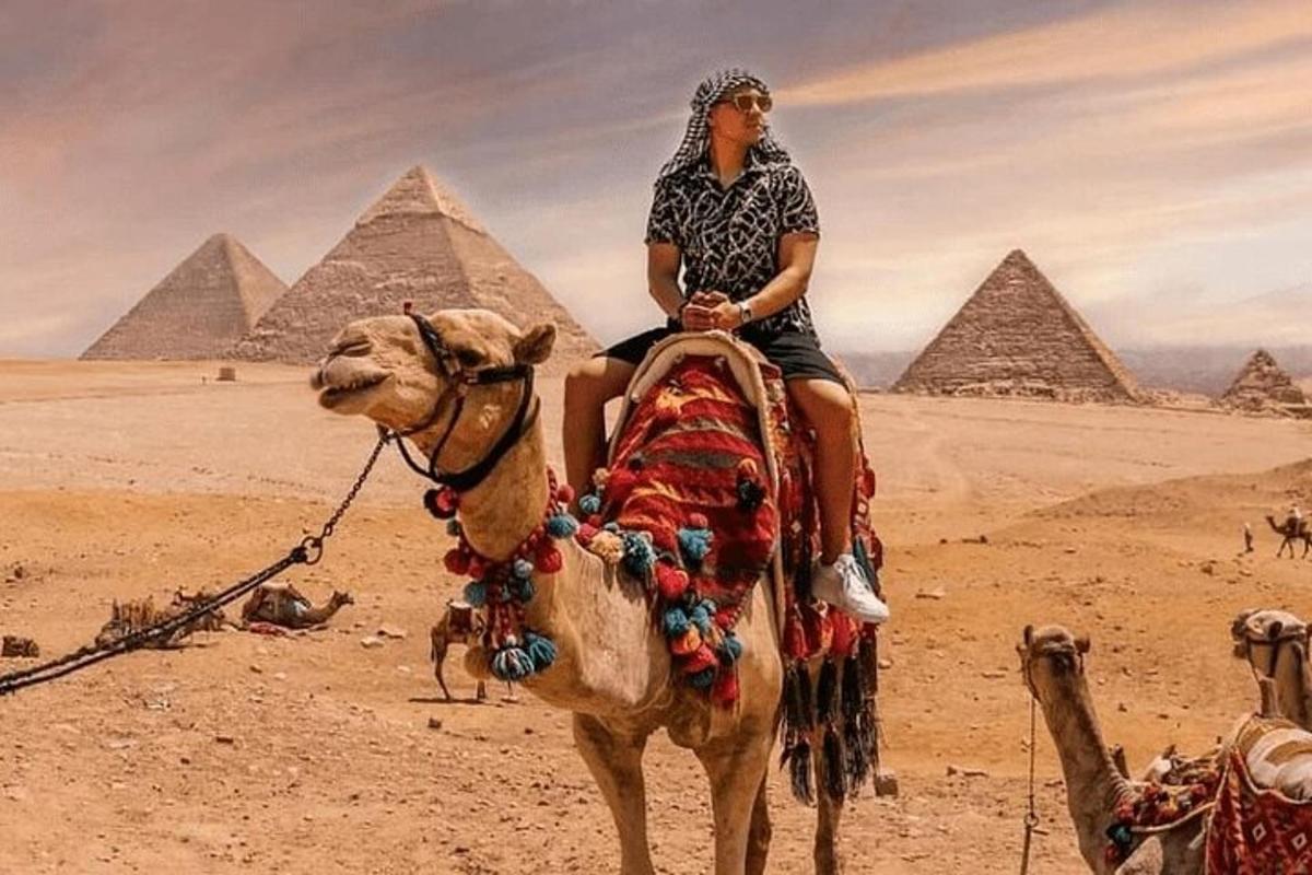 muž jedoucí na velbloudovi před pyramidami