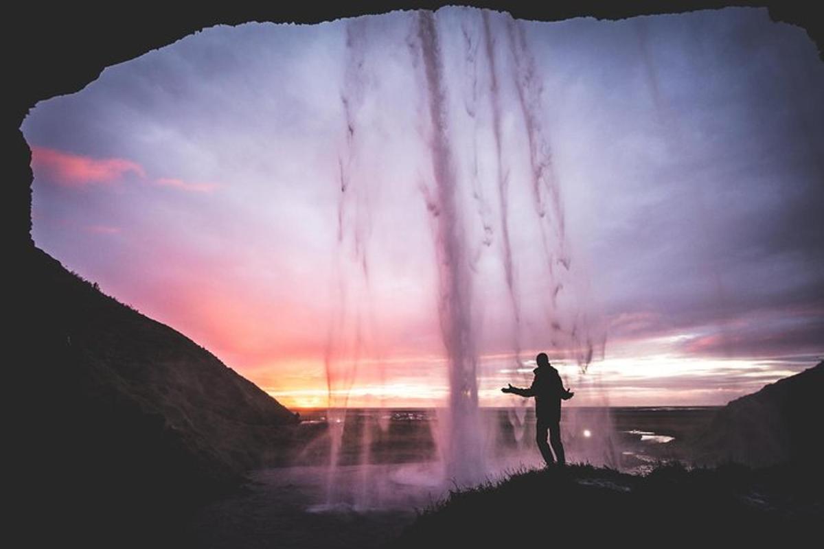 a man standing in front of a waterfall at sunset