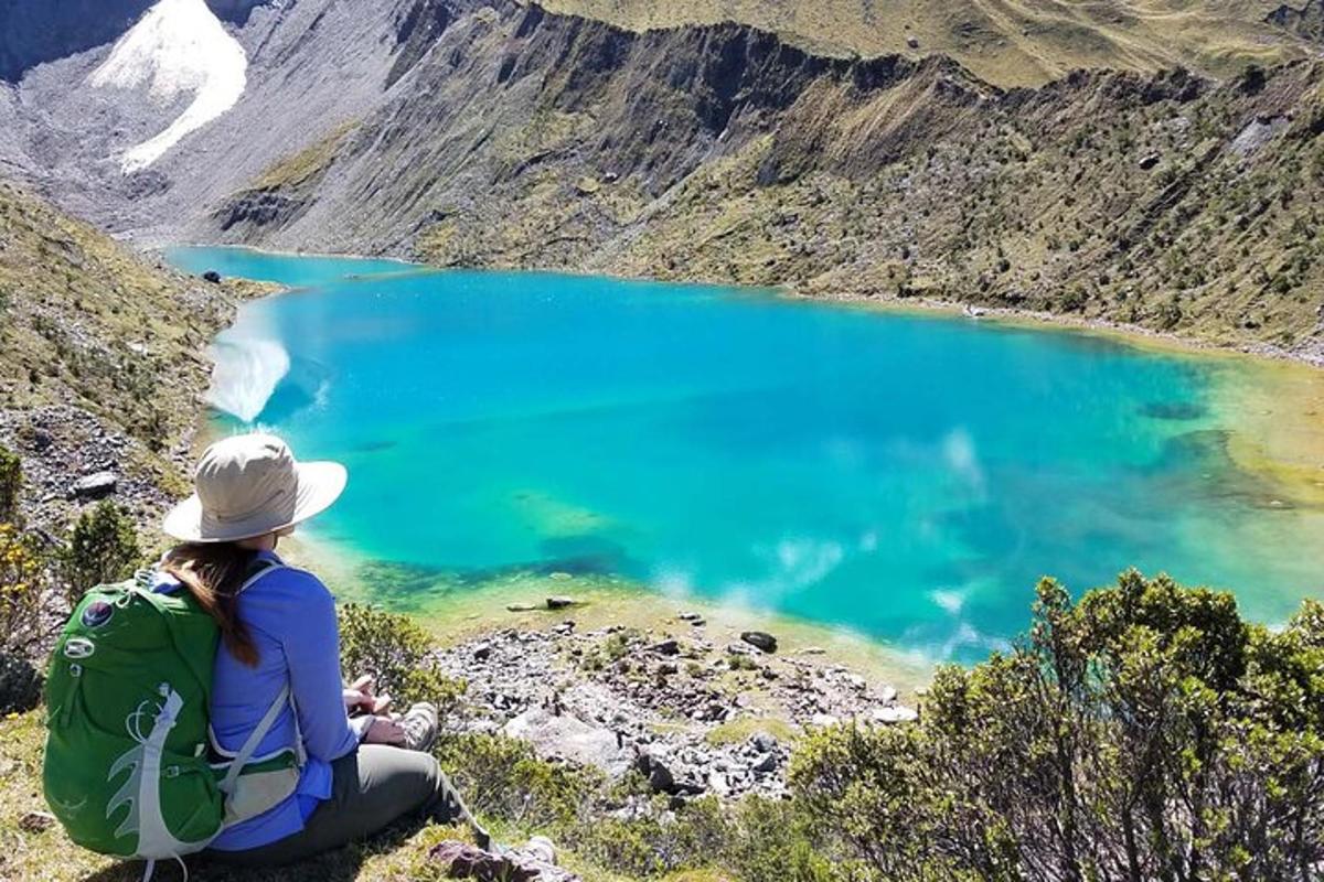 eine Frau, die auf einem Berg sitzt und auf einen blauen See blickt