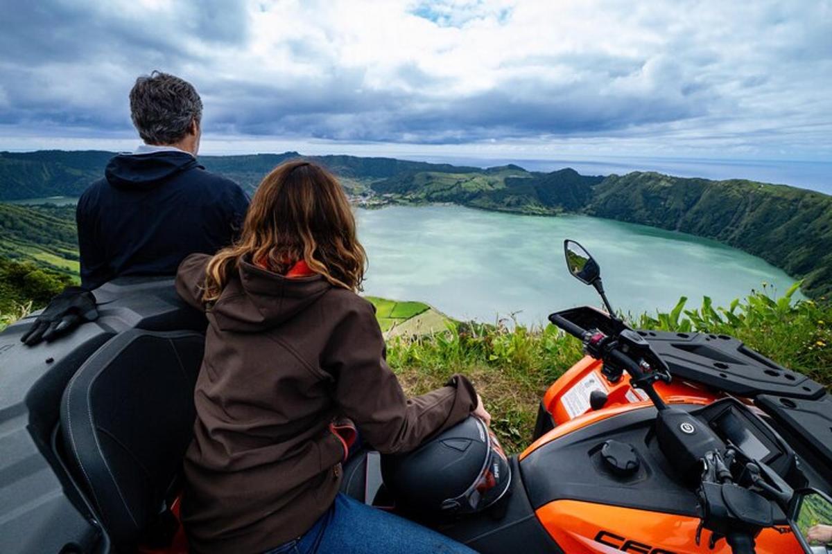 a man and woman sitting on a motorcycle overlooking a lake