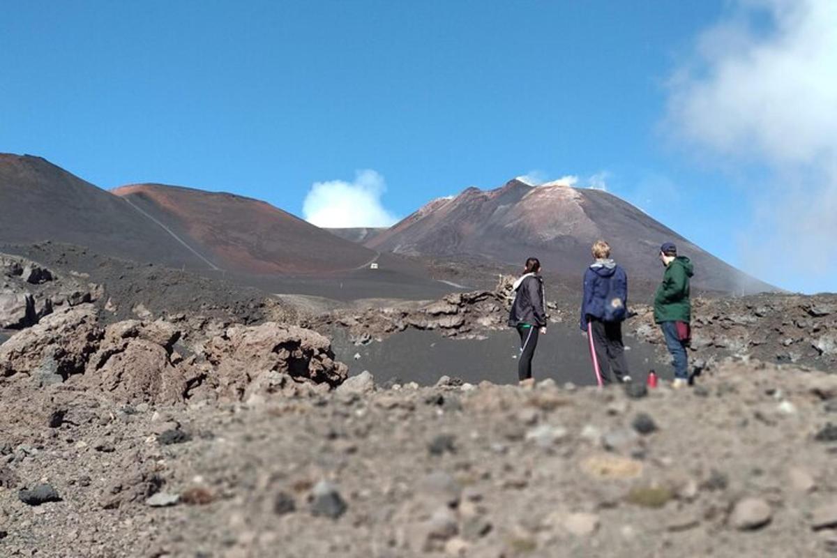 tiga orang berdiri di atas bukit berbatu dengan latar belakang gunung