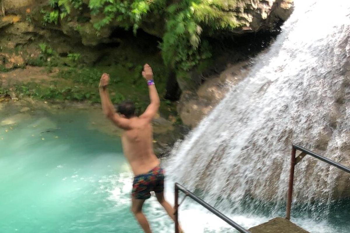 Un hombre parado en un charco de agua junto a una cascada.