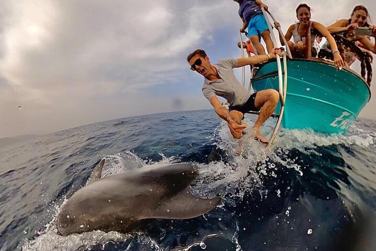 a group of people on a boat with a dolphin in the water