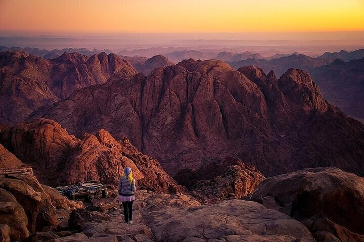 uma pessoa em pé no topo de uma montanha ao pôr do sol