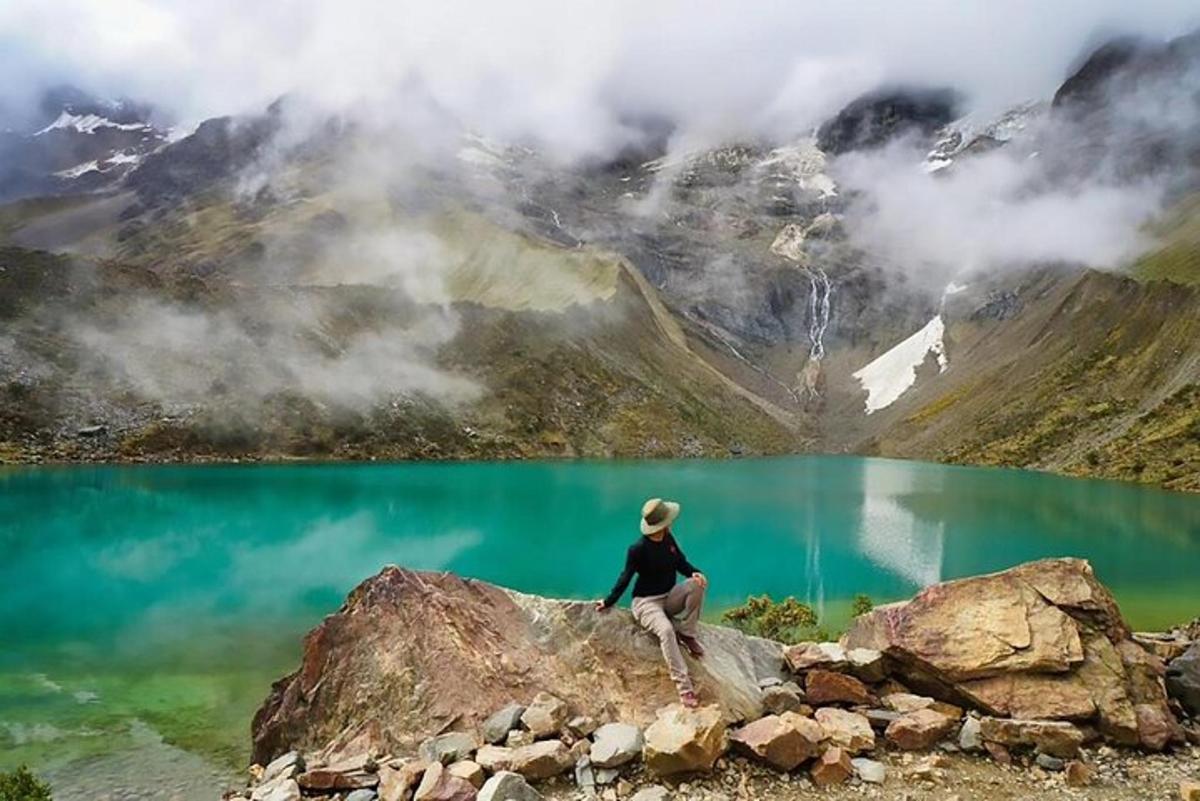 una persona sentada en una roca con vistas a un lago de montaña