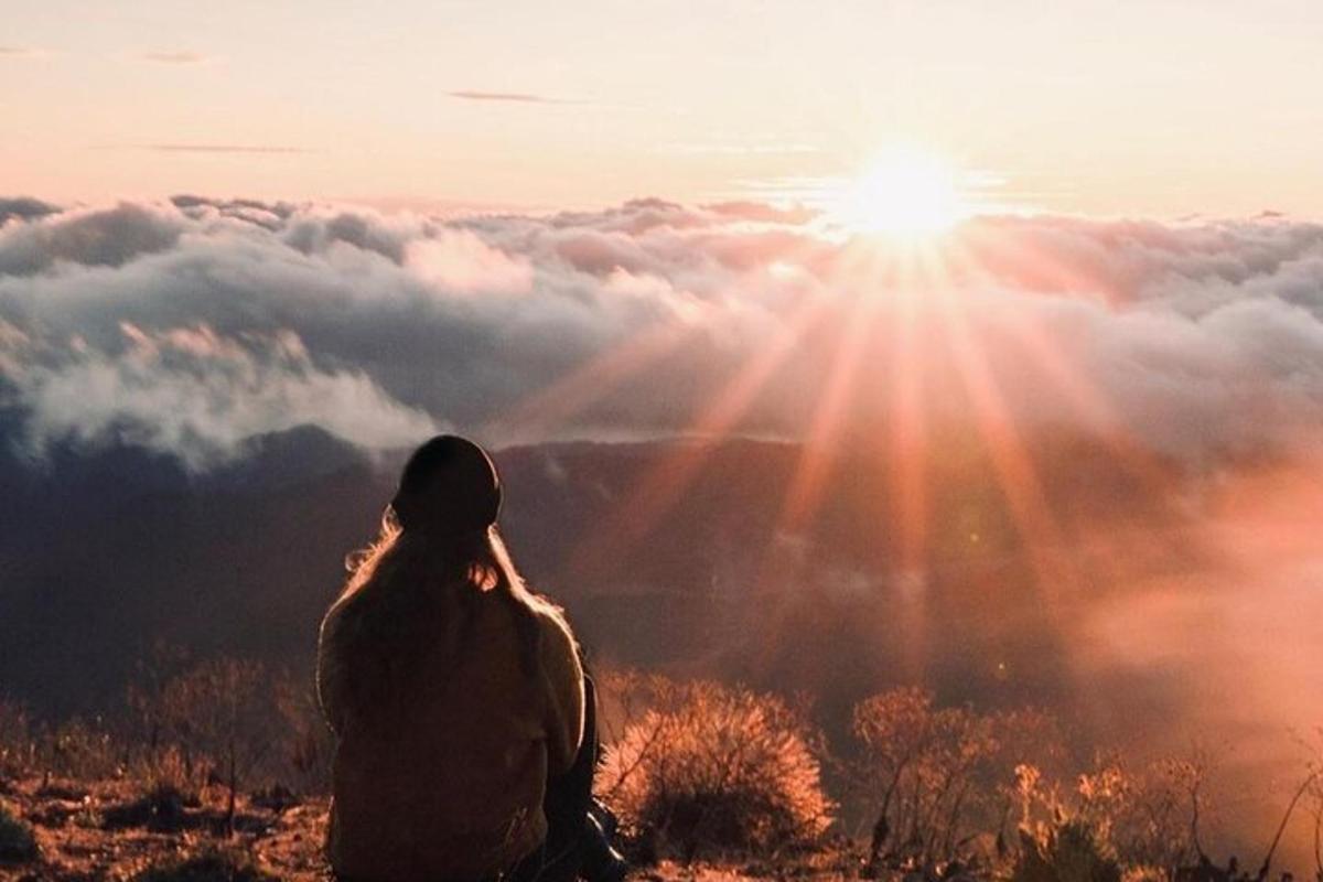Una mujer sentada en la cima de una montaña mirando la puesta de sol