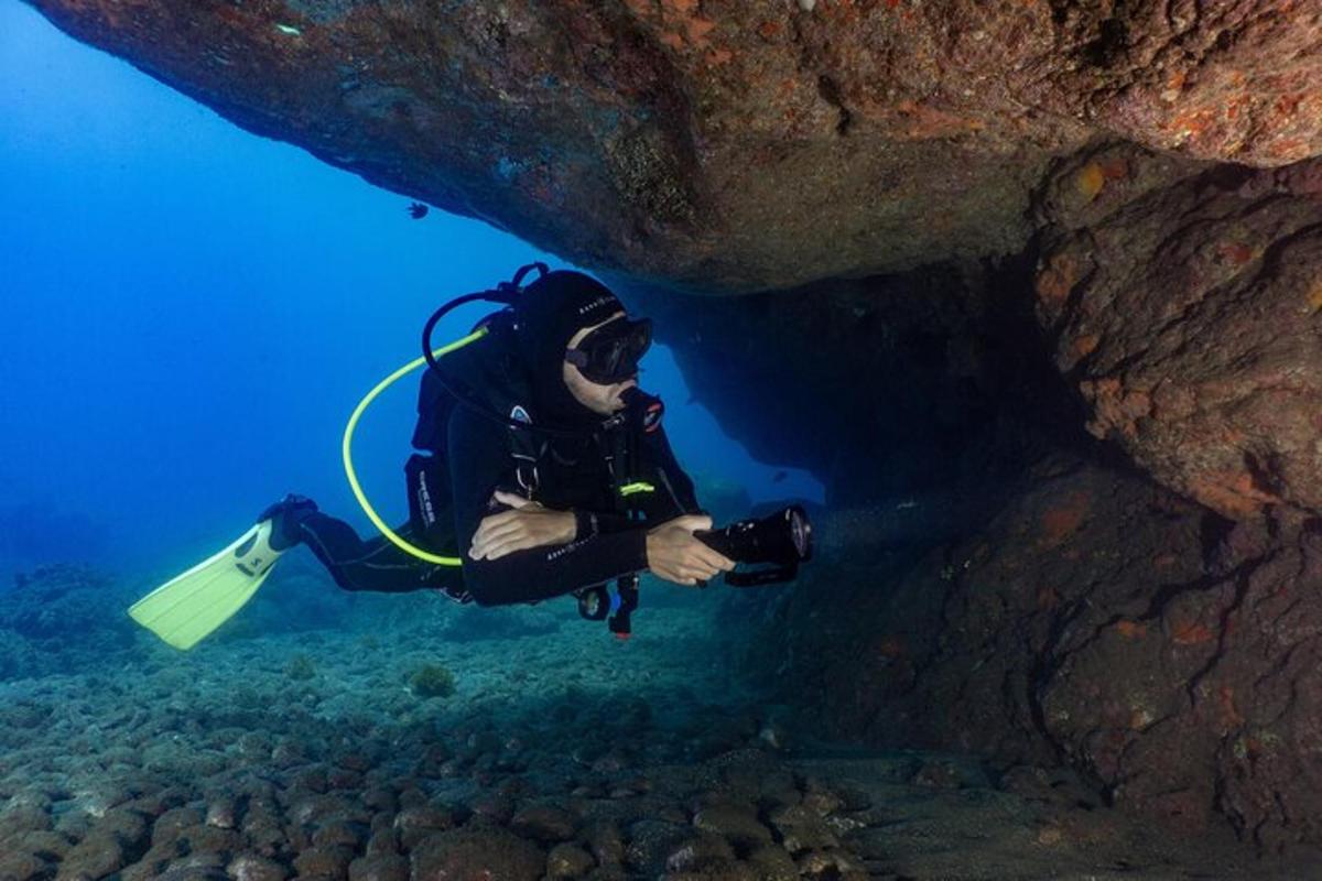 um homem em um traje de mergulho segurando uma câmera em uma caverna
