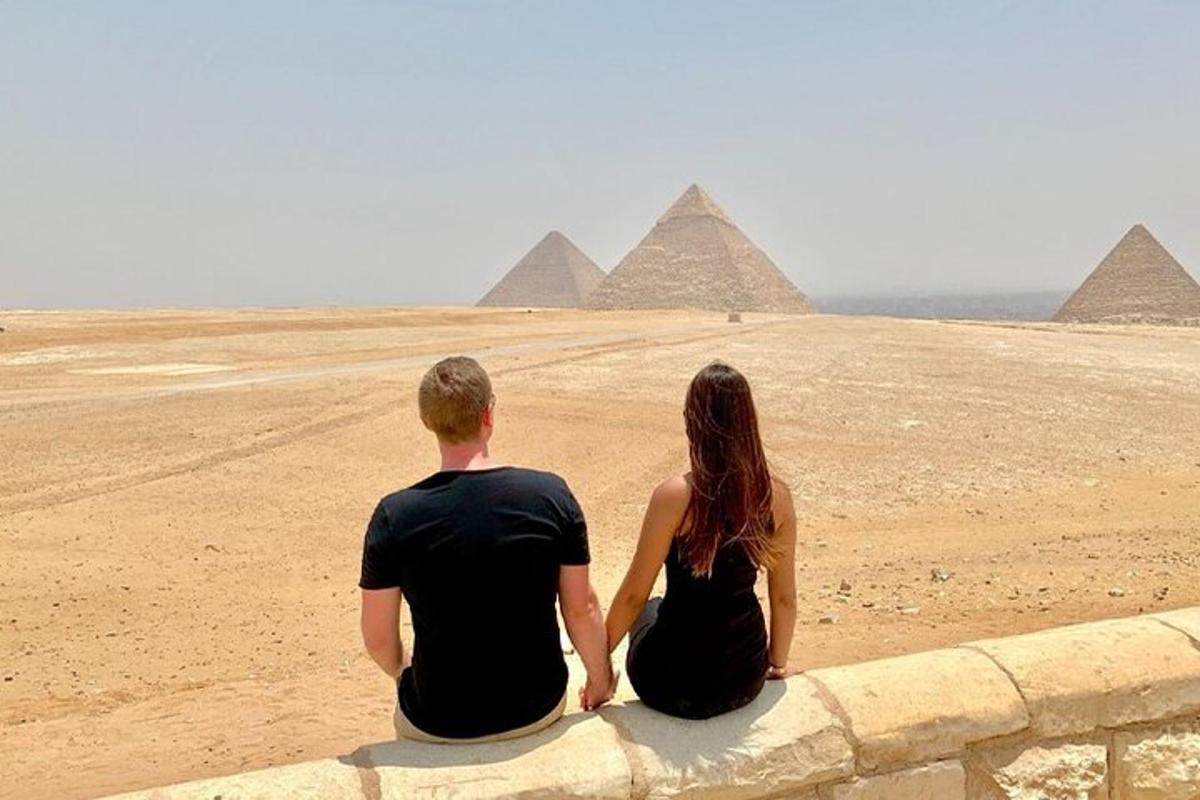 رجل وامرأة يجلسان على الحائط ينظران إلى الأهرامات