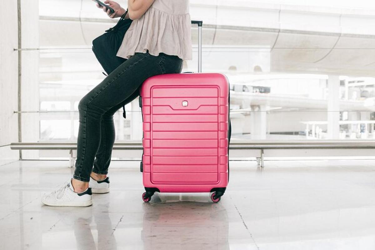 en kvinne trekker en rosa koffert på en flyplass