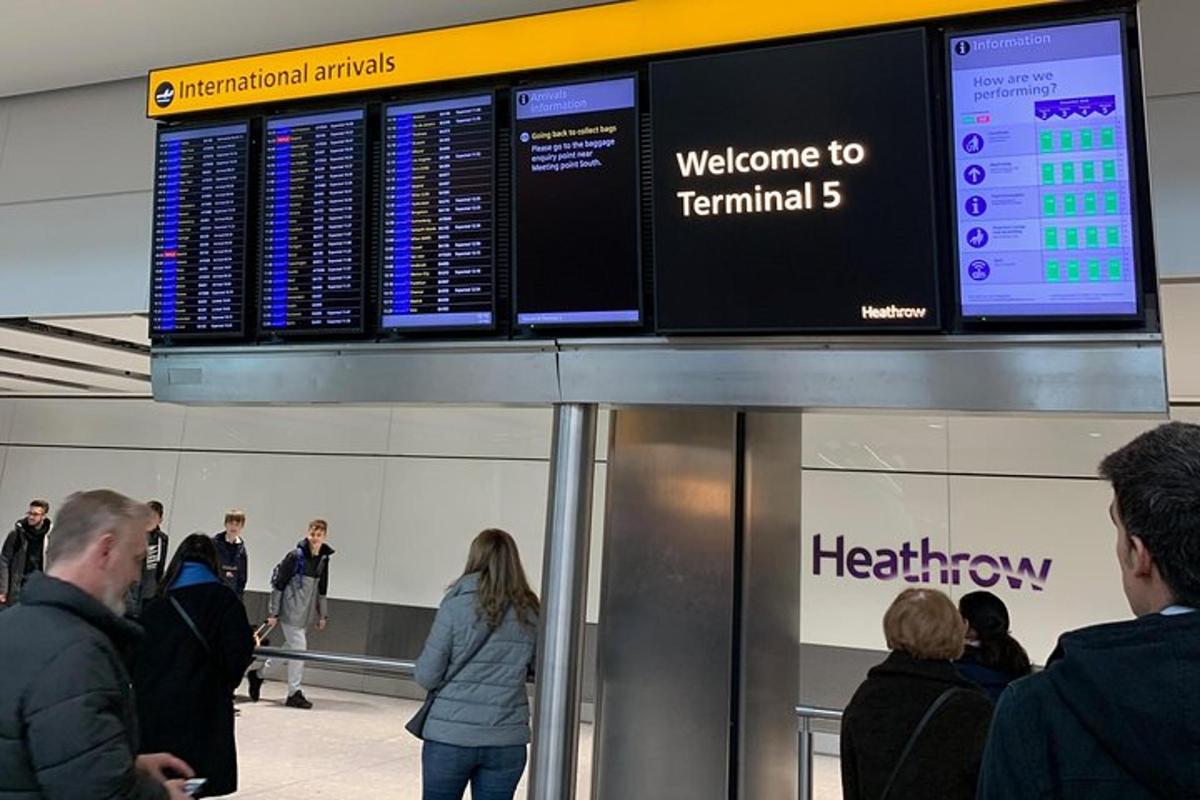 people waiting at an airport with a departure board