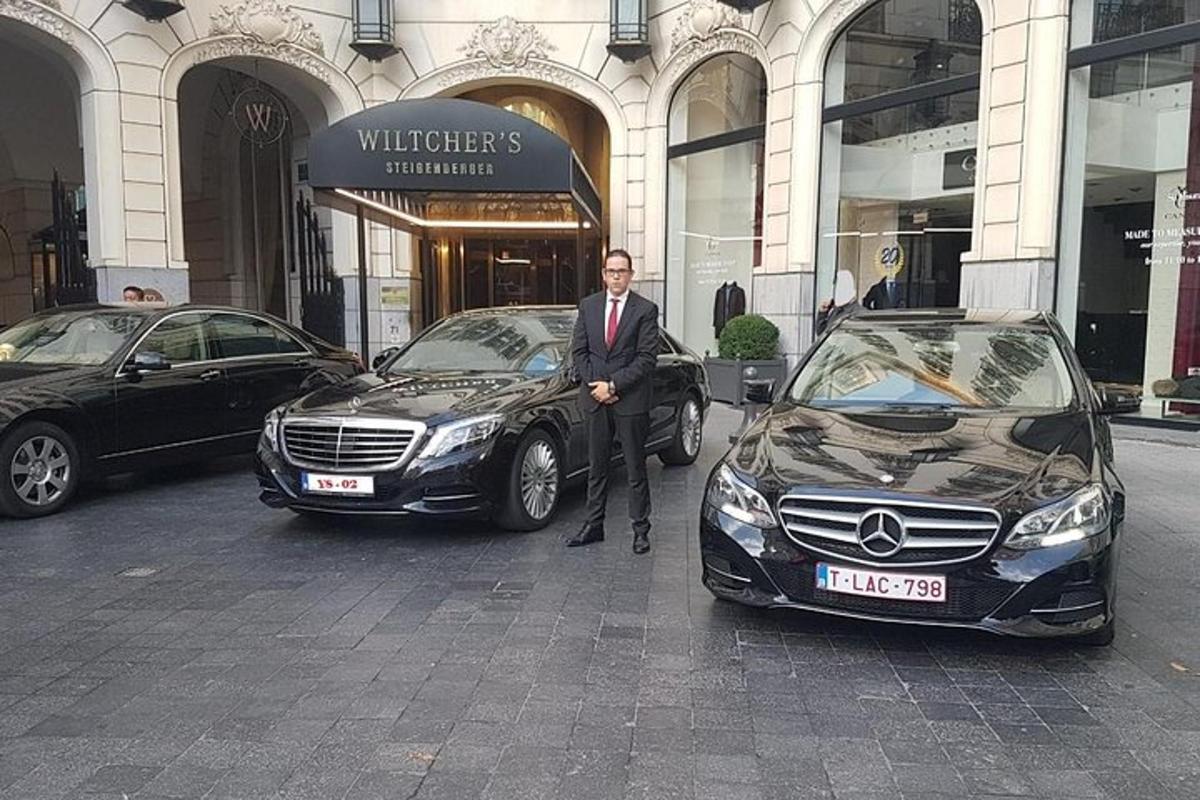Un hombre con traje de pie junto a dos coches.