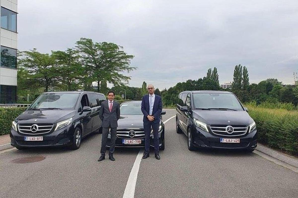 Dos hombres parados en un estacionamiento junto a dos autos.
