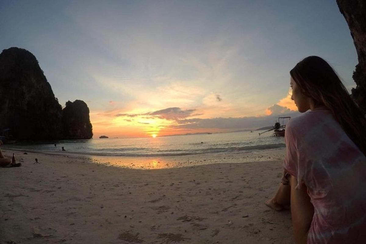 seorang wanita duduk di pantai melihat matahari terbenam