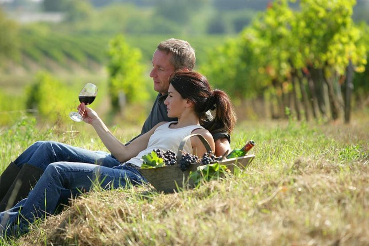 a man and woman sitting in a field with a glass of wine