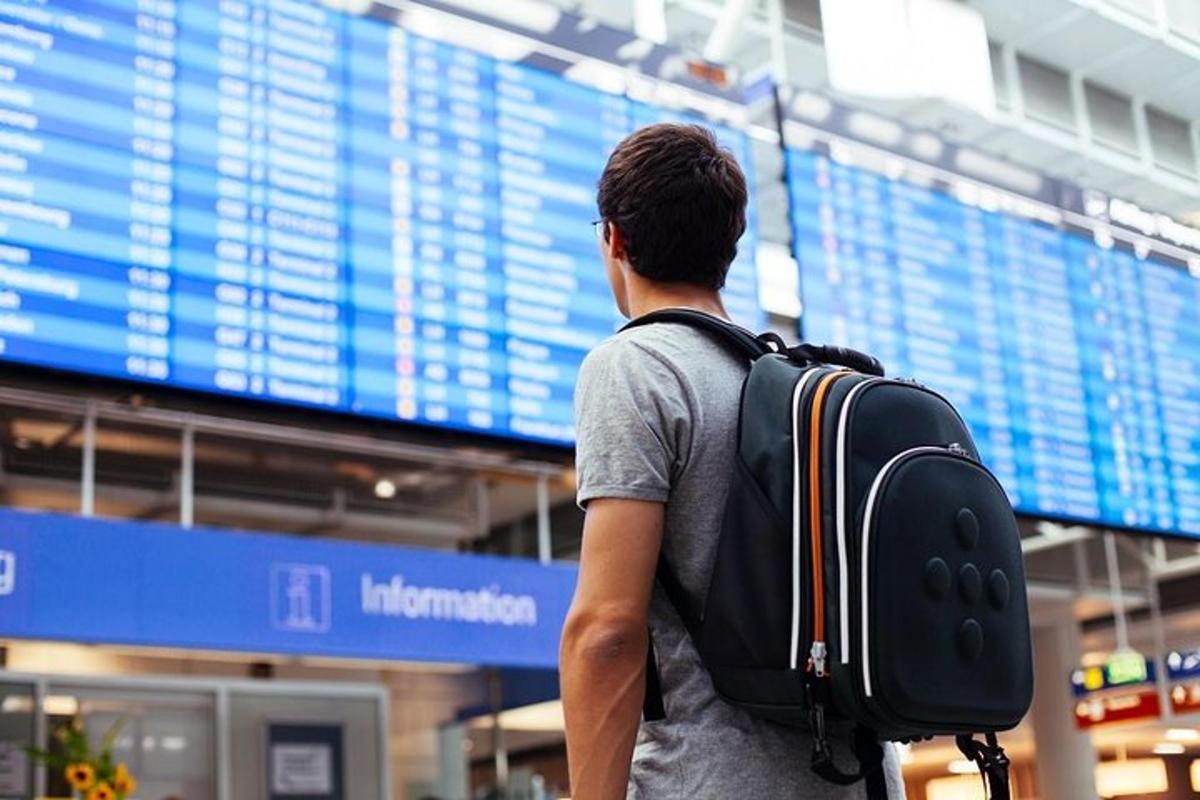 Un hombre con una mochila de pie frente a un aeropuerto.