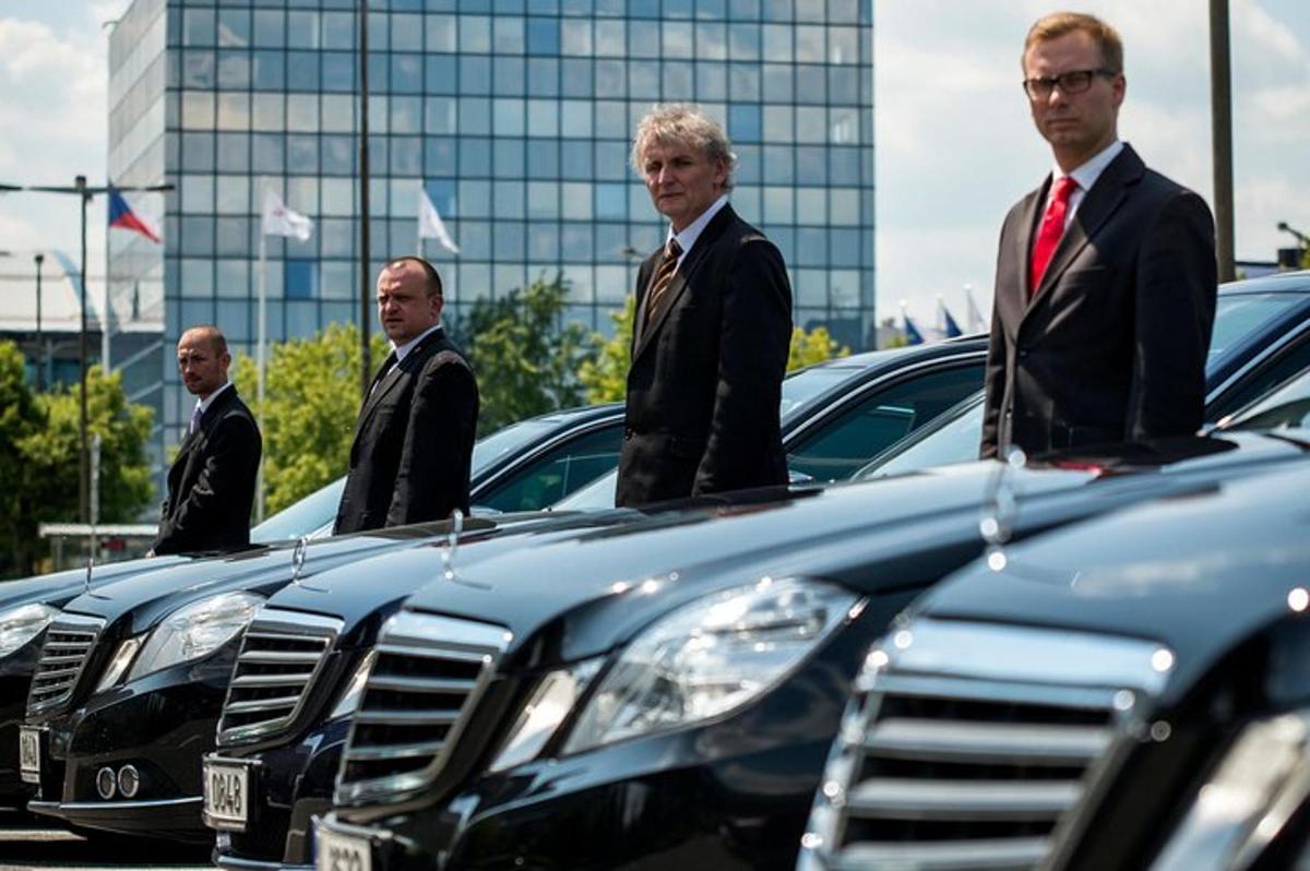 skupina mužov v oblekoch stojacich vedľa radu áut