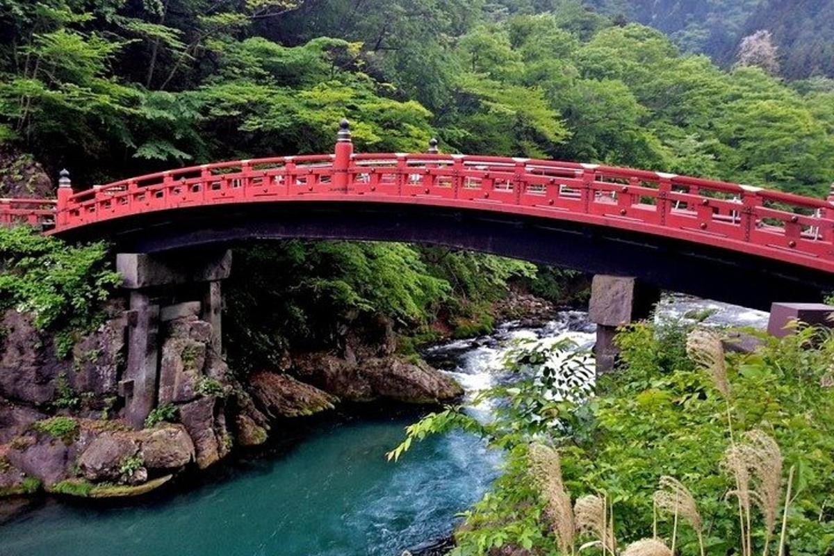 a red bridge over a river next to a mountain