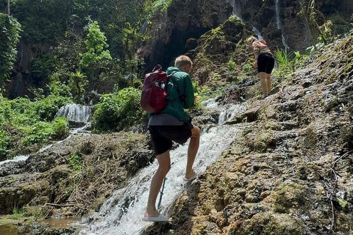 two people walking on a rocky trail near a waterfall