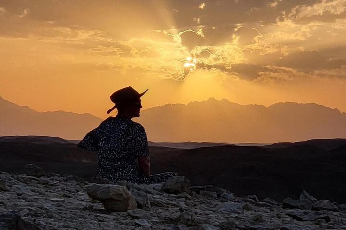 una persona sentada en el desierto mirando la puesta de sol