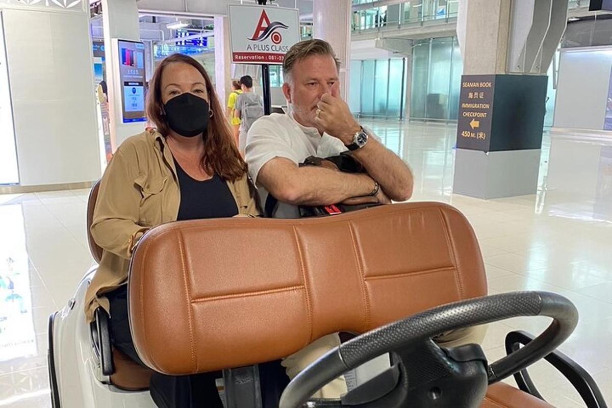 muž a žena sedící v zavazadlovém vozíku na letišti