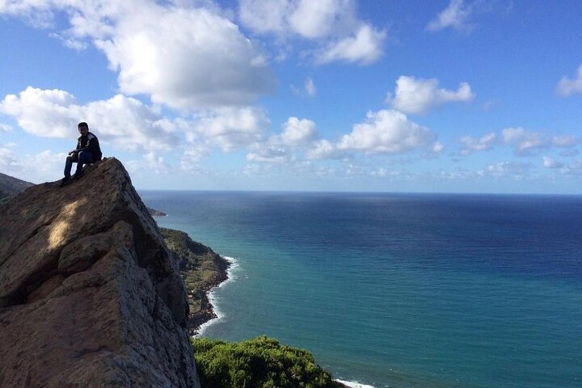 un home assegut a dalt d'una roca amb vistes a l'oceà