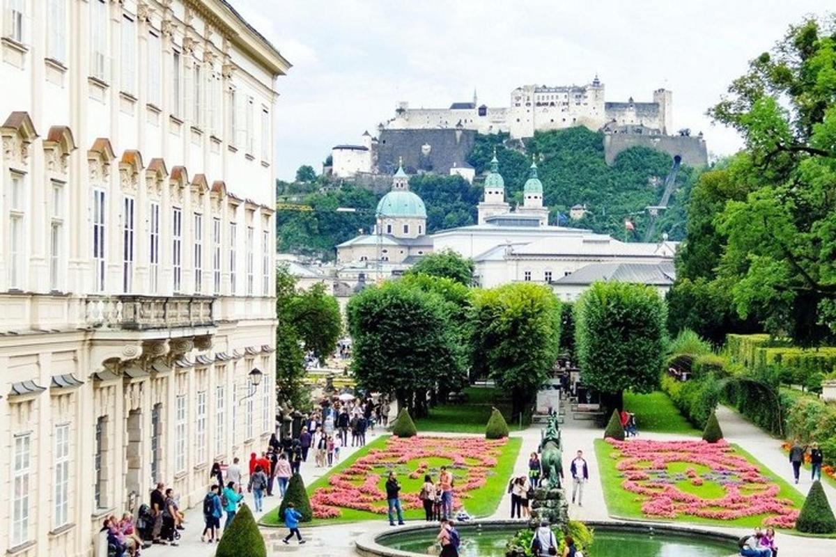 a crowd of people walking around a fountain in a park with a castle in