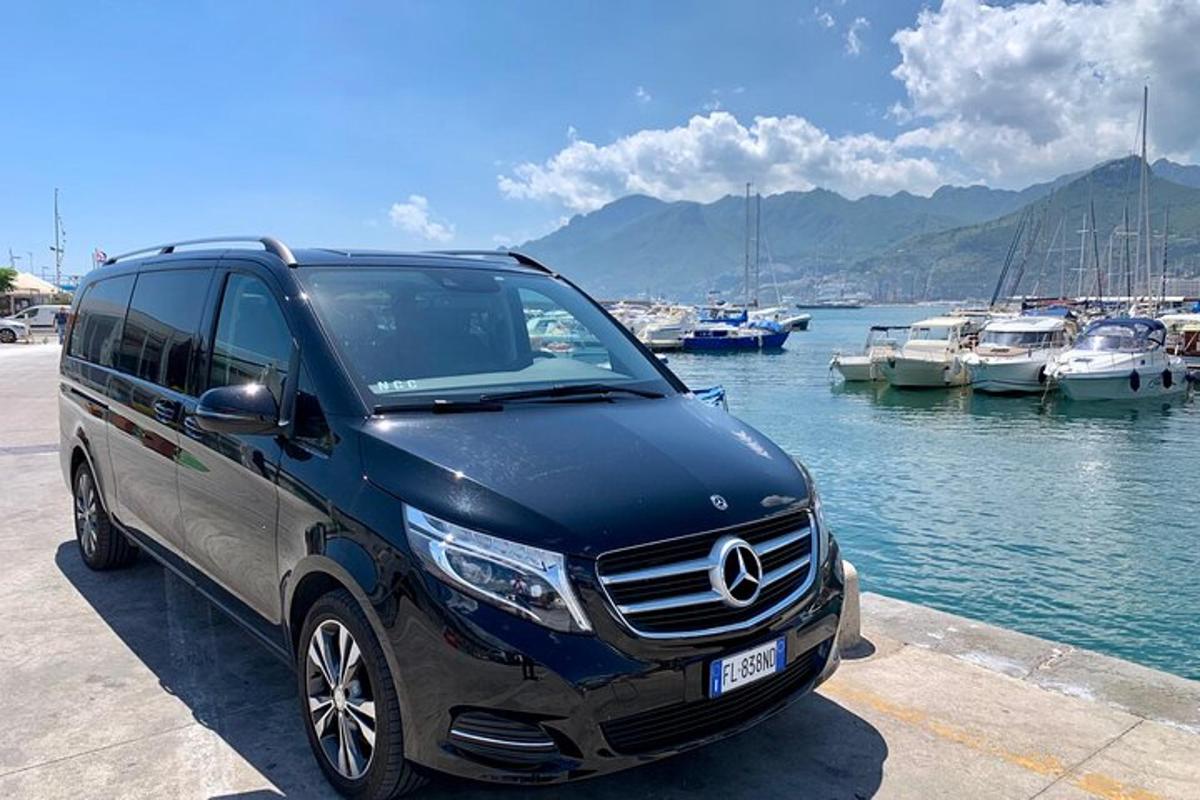 Blár Mercedes Benz jeppabíll lagður við smábátahöfn