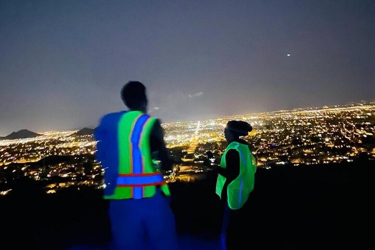 due persone in piedi su una collina che guardano una città di notte