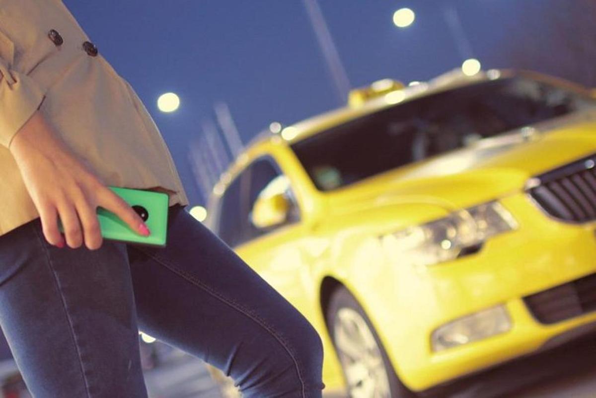 o persoană care ține un telefon mobil în fața unui taxi