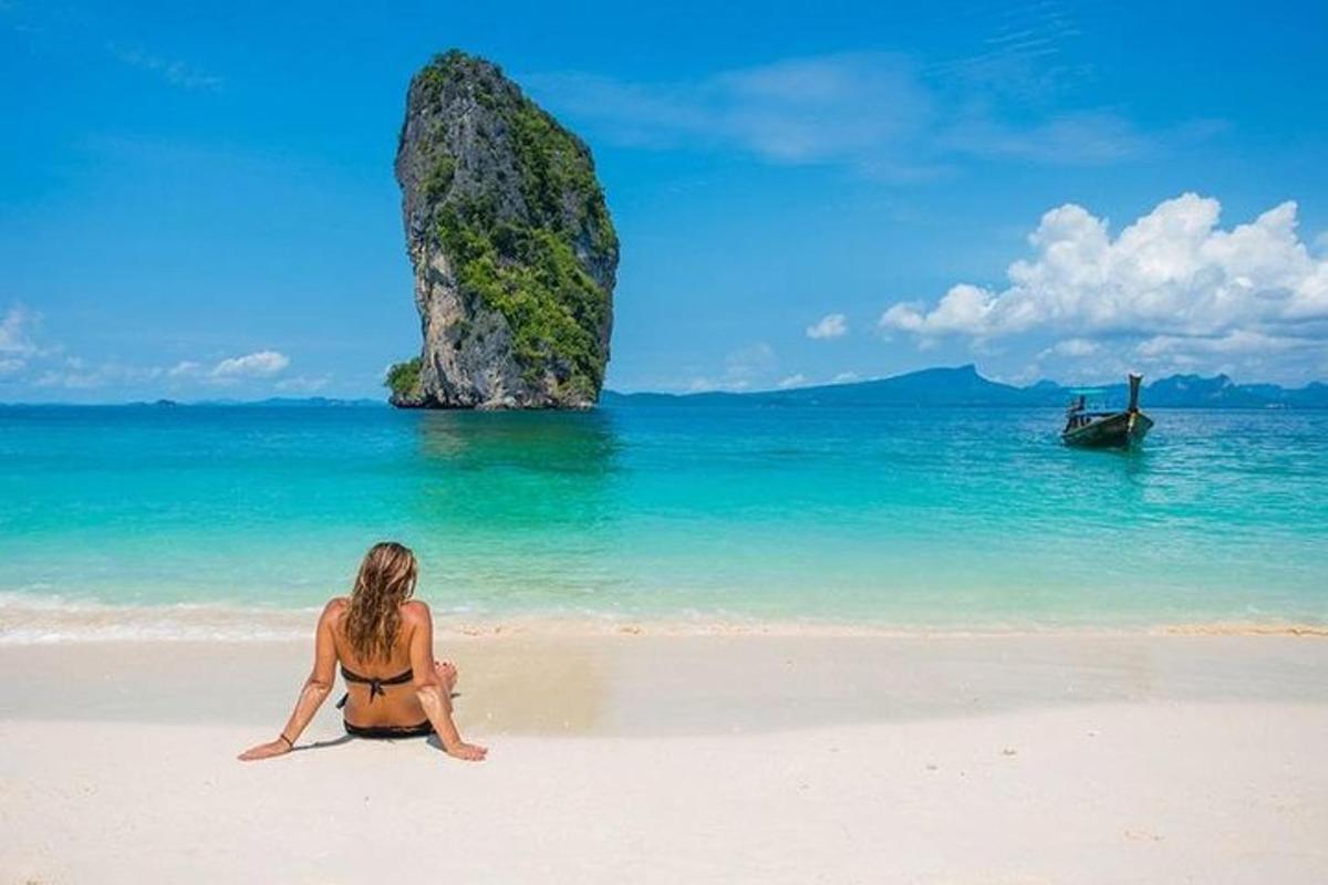 Una mujer sentada en una playa con una roca en el océano.