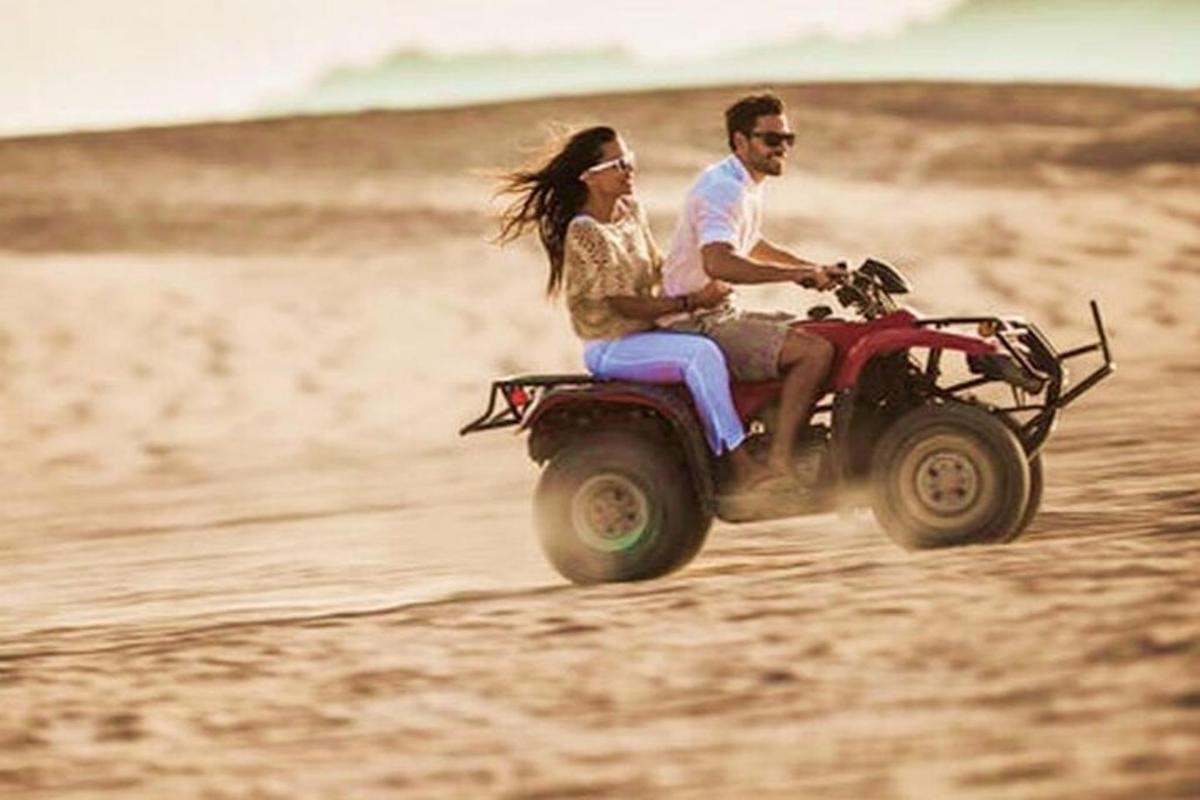 Un hombre y una mujer viajando en un quad por la playa