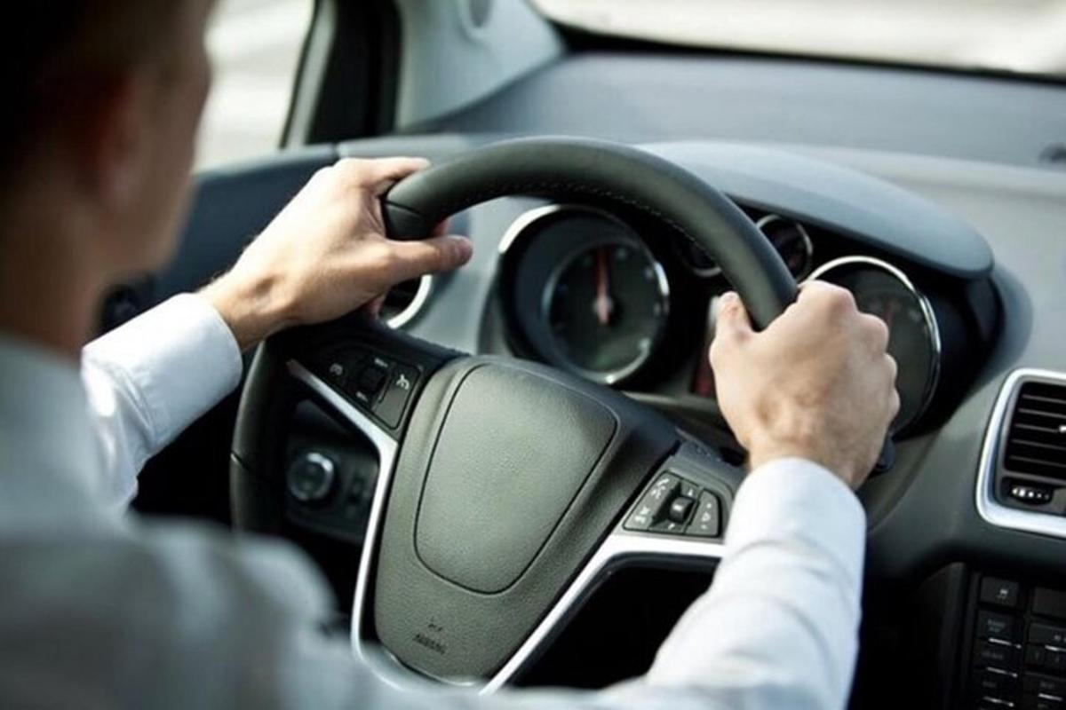 muž řídící auto s rukama na volantu