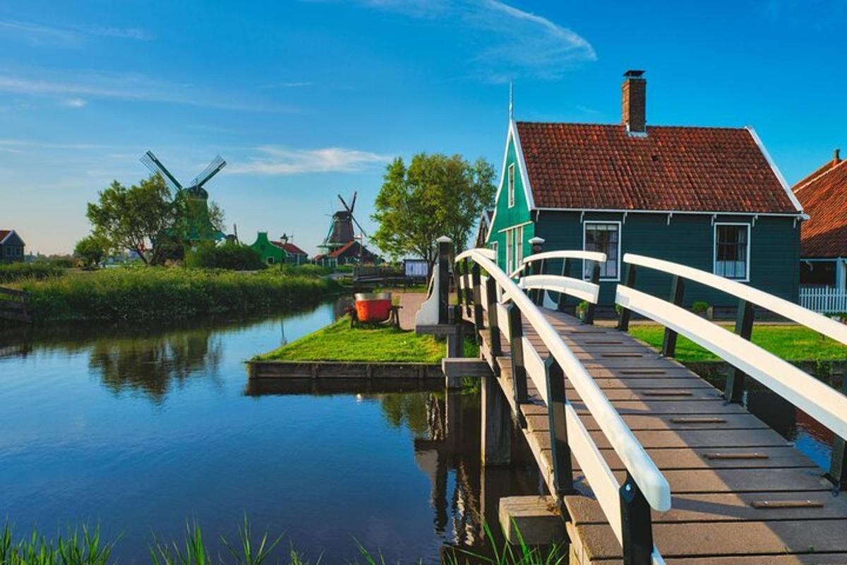 a blue house with a bridge next to a river with windmills