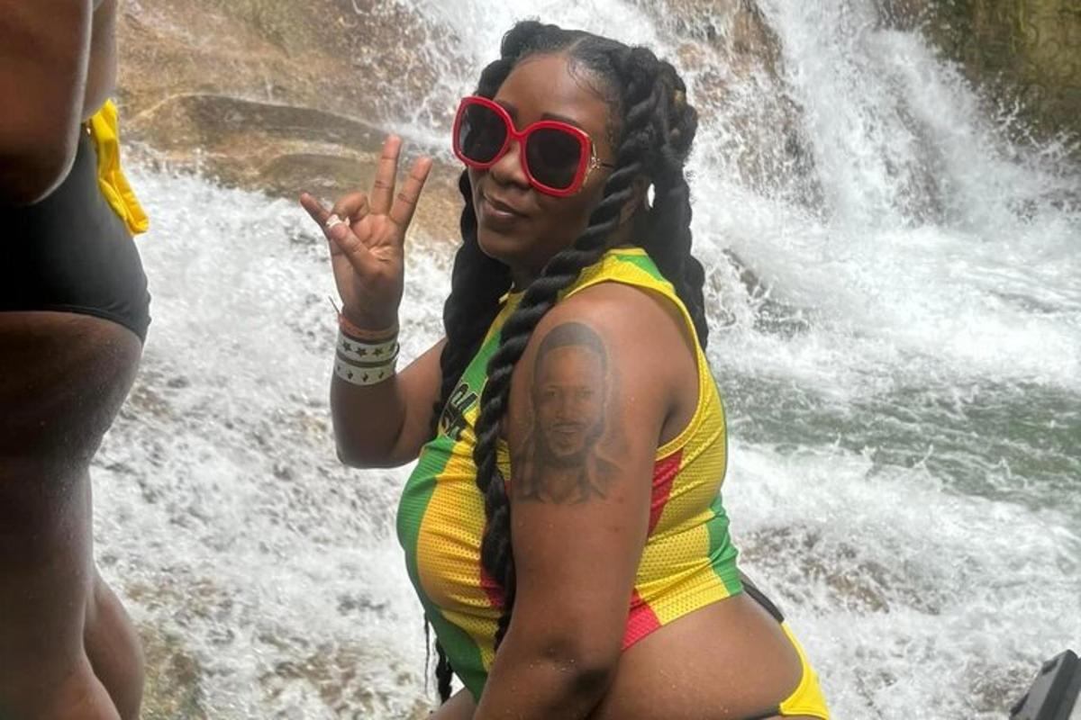seorang wanita berkaca mata hitam duduk di hadapan air terjun