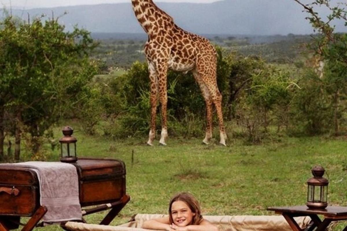 uma girafa em pé ao lado de uma mulher deitada na frente de uma girafa