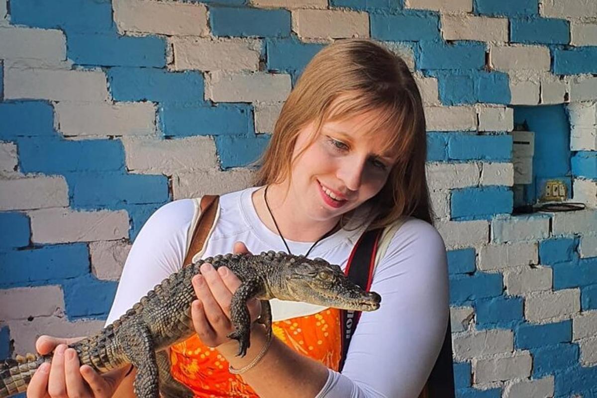 eine Frau, die einen Alligator vor einer Wand hält