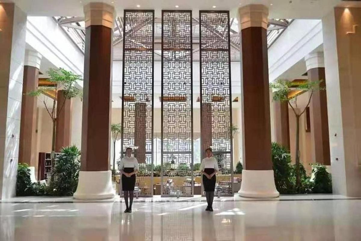 three people walking in a lobby with a large window