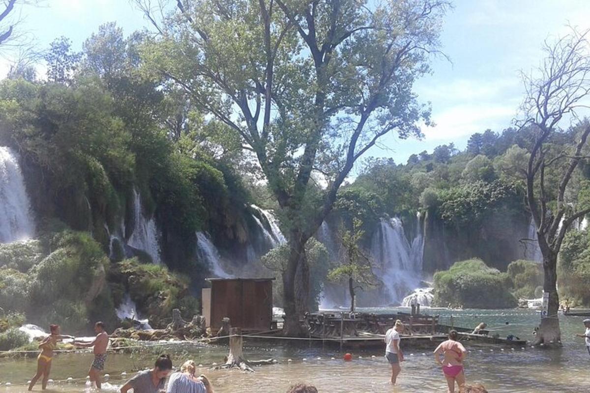 Personas paradas en el agua frente a una cascada.