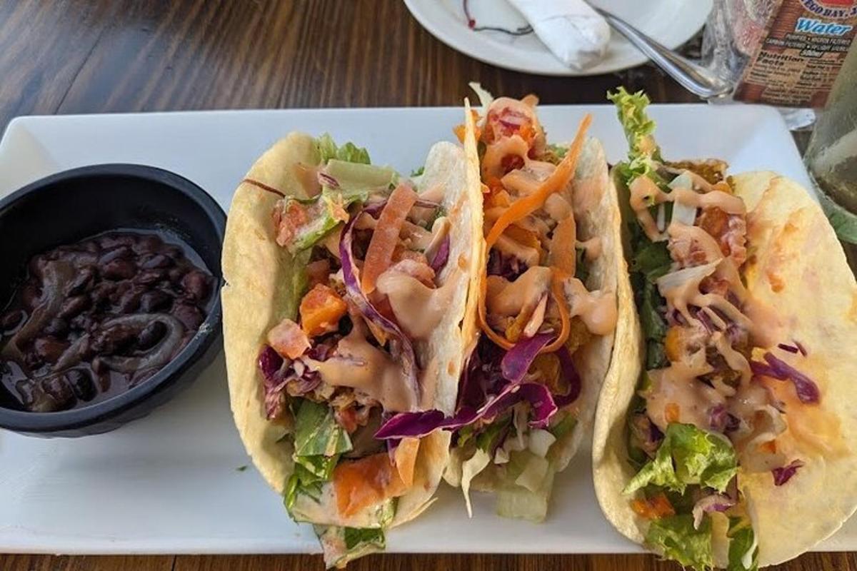 ein weißer Teller mit zwei Tacos und einer Schüssel Dips