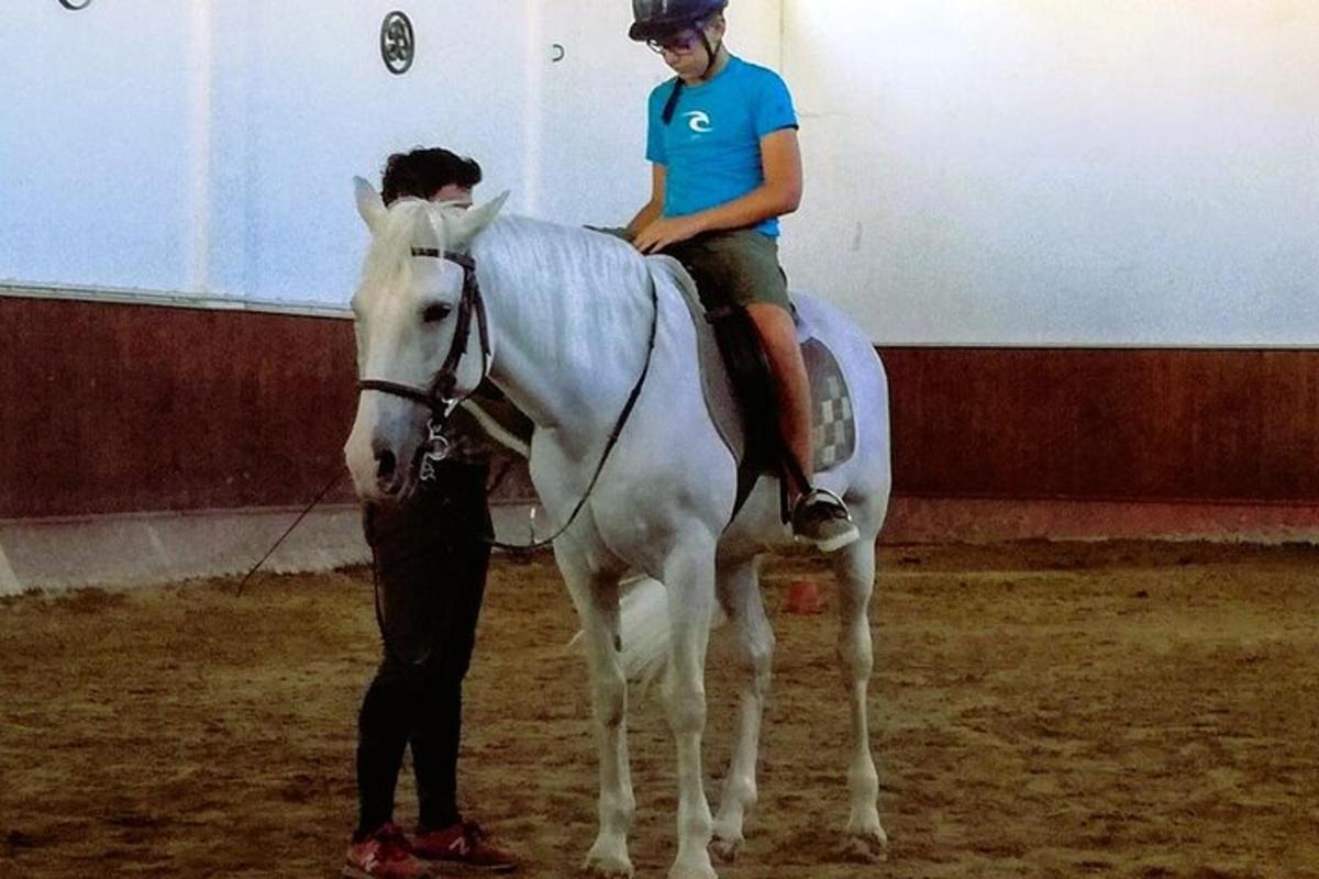 Un hombre sentado en un caballo blanco junto a una persona.