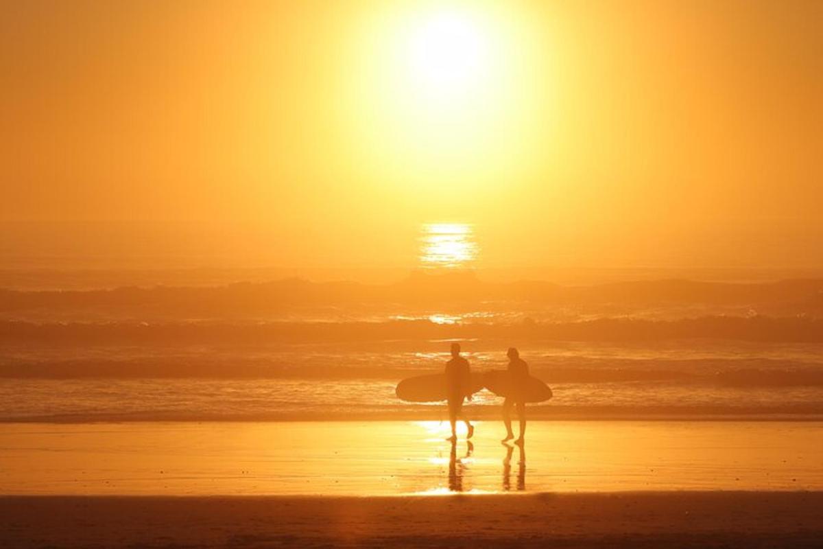 Dos personas de pie en la playa al atardecer con tablas de surf