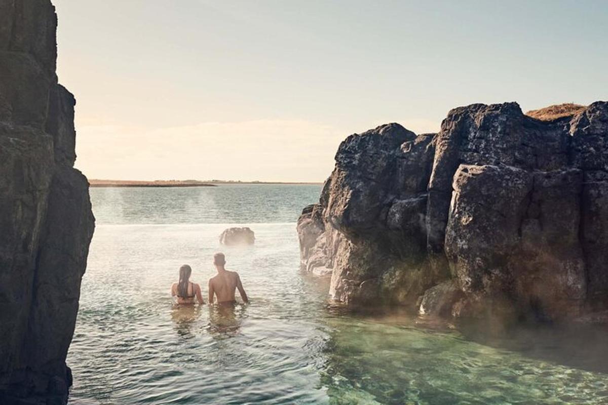 two people sitting in the water near some rocks