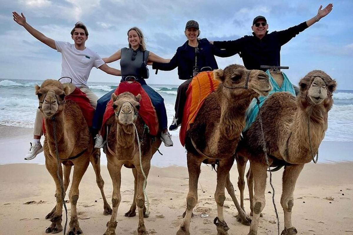 Un grupo de personas montando camellos en la playa.