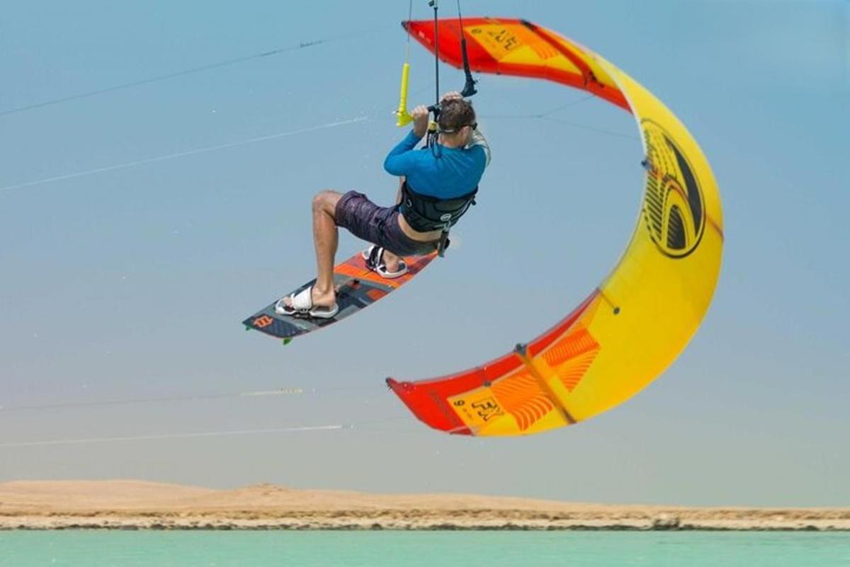 osoba jedoucí na windsurfingu a držící se padáku