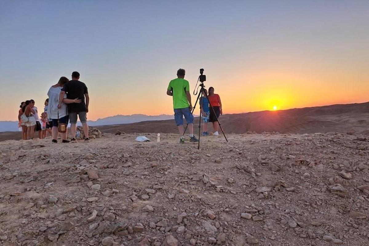 eine Gruppe von Menschen steht auf einem Berg und beobachtet den Sonnenuntergang