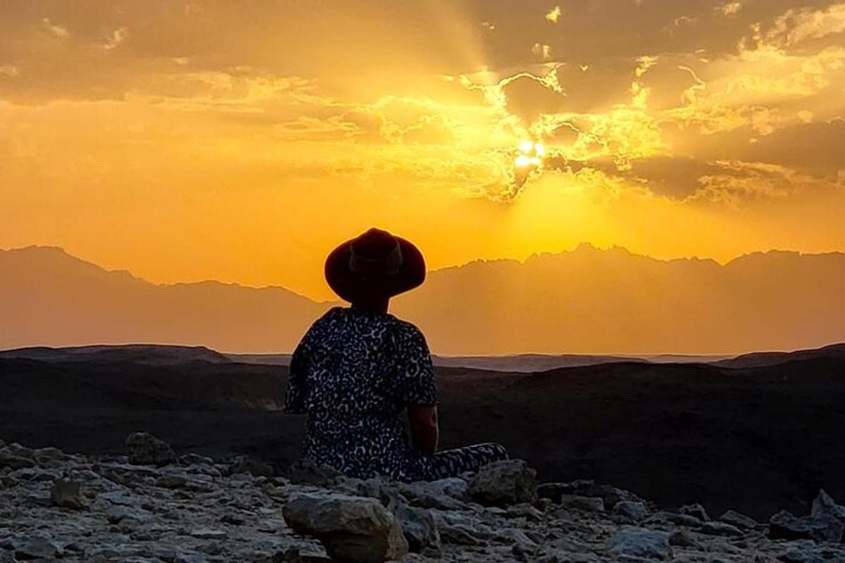شخص يجلس على الصخور يشاهد غروب الشمس